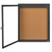 A brown cork bulletin board with a black frame and a door open.