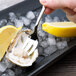 A person holding a Chef & Sommelier stainless steel oyster fork over a lemon wedge on ice.