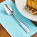 A Choice Bellwood stainless steel teaspoon on a napkin next to a slice of pumpkin pie.