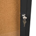 An Aarco black metal enclosed bulletin board cabinet with a key lock on a door.