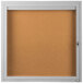 A white framed bulletin board with a glass door and key lock.