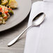 A Chef & Sommelier stainless steel teaspoon on a napkin next to a plate of food.