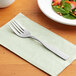A Choice Delmont stainless steel salad fork on a napkin next to a plate of salad.
