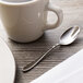A Chef & Sommelier stainless steel demitasse spoon on a table next to a white cup and saucer.