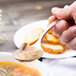 A hand holding a Chef & Sommelier stainless steel soup spoon over a bowl of soup.