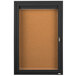 A black indoor lighted bulletin board cabinet with a cork board and a key.