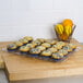 A Cal-Mil shallow clear bakery tray holding blueberry muffins on a counter.