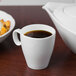 A Schonwald white porcelain espresso cup filled with coffee on a counter next to a bowl of food.
