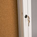 A white Aarco indoor bulletin board cabinet with a key in the door lock.