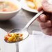 A hand holding a Chef & Sommelier stainless steel dinner spoon with food.