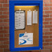 An Aarco blue indoor bulletin board cabinet with a sign on it.