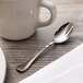 A Chef & Sommelier stainless steel demitasse spoon on a table next to a white mug.