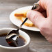 A hand holding a Chef & Sommelier stainless steel demitasse spoon over a cup of coffee.