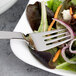 An Arcoroc stainless steel salad fork in a salad on a plate.