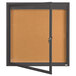 An Aarco bronze anodized indoor bulletin board with a cork surface and glass door.