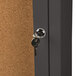 The bronze door of an Aarco lighted bulletin board cabinet with a key in the lock.