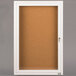 A white cabinet with a cork board and glass door with a key.