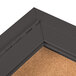 A close-up of the corner of an Aarco bronze anodized indoor bulletin board cabinet with cork board inside.