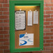 An Aarco green powder coated bulletin board cabinet with a light inside.