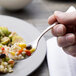 A hand holding a Chef & Sommelier stainless steel spoon with food on it.