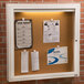 A white cork bulletin board with papers pinned to it inside a cabinet with a door.