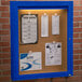 An Aarco blue indoor bulletin board cabinet with paper pinned to it.