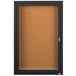 A black Aarco enclosed bulletin board cabinet with a cork board inside and a key lock.