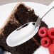 An Arcoroc stainless steel dessert spoon on a plate with a piece of cake and raspberries.