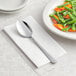 A white plate of vegetables with a Choice Windsor stainless steel serving spoon on a napkin.