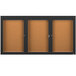A brown rectangular bulletin board cabinet with a black border and three black doors with glass panels.