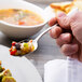 A hand holding a Chef & Sommelier stainless steel teaspoon full of food over a plate.