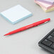 A red Paper Mate Flair pen next to a stack of sticky notes.