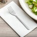 A Choice Dominion stainless steel salad fork on a white napkin next to a bowl of salad.