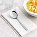 A Choice Windsor stainless steel bouillon spoon in a bowl of soup on a napkin.