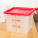 A translucent square Cambro food storage container with a red lid.