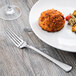 A Libbey stainless steel dinner fork on a plate of food with a meatball.