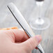 A hand holding a Libbey stainless steel utility fork and knife over a wine glass.