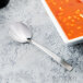A Libbey stainless steel bouillon spoon next to a bowl of soup.