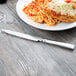 A Libbey stainless steel dinner knife on a wooden table with a plate of food.