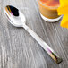 A Libbey stainless steel dessert spoon in a glass of liquid on a table.