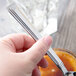 A person holding a Libbey stainless steel dessert spoon over a jar of sauce.