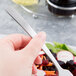 A hand holding a Libbey Oceanside stainless steel salad fork over a salad.