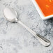 A Libbey stainless steel round bowl soup spoon next to a bowl of soup.