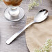 A Libbey stainless steel dessert spoon on a table next to a glass of ice cream.