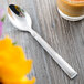 A Libbey stainless steel teaspoon with a slate handle on a table next to a cup of coffee.