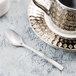 A Libbey stainless steel demitasse spoon on a white plate with a silver cup and saucer.