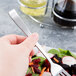 A hand holding a Libbey New Charm stainless steel salad fork over a salad.
