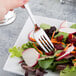 A Libbey stainless steel salad fork spearing vegetables on a plate of salad.