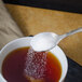 A Master's Gauge stainless steel demitasse spoon pouring sugar into a cup of tea.