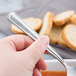A hand holding a Libbey stainless steel bouillon spoon.